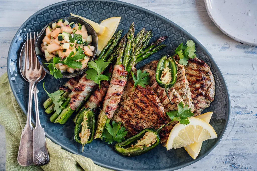 Grillattu maatiaispossun chimichurri fileepihvi, cantaloupe-kesäkurpitsasalsa ja pekoniin käärityt parsat